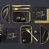 A flat lay arrangement of New Year's Eve themed party supplies, including black and gold plates, napkins, cutlery, and decorative spheres. Produktbild-Vorschau