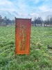 A rusted metal garden screen with a bamboo motif stands in a grassy field under a cloudy sky. Produktbild-Vorschau
