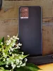 A close-up shot of the back of a black smartphone with a camera module, placed next to a bouquet of small white flowers and green leaves. Produktbild-Vorschau