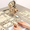 A wooden model of a film projector is assembled on a table with various parts and instructions. Produktbild-Vorschau
