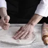 A person's hands are shown kneading dough on a surface, with a rolling pin to the side. Produktbild-Vorschau