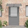A gray door with a polycarbonate awning above it, set against a brick wall. Voir les images du produit