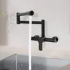 A black wall-mounted kitchen faucet with water flowing into a stainless steel sink. Podgląd zdjęcia produktu