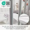 Close-up view of a crib with a white mattress protector and a tag indicating Oeko-Tex certification. Produktbild-Vorschau