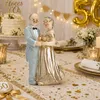Dekorative Tischszene zur goldenen Hochzeit mit Tortenaufsatz eines älteren Ehepaares, goldenen Accessoires, Kerzen und festlicher Dekoration. Anteprima dell’immagine prodotto