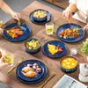 A table setting with a 12-piece stoneware dinnerware set for 4 people, featuring plates, bowls, and food items like croissants, salad, and soup. Produktbild-Vorschau