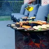A person is pouring oil onto a grill with various foods cooking on it, in a backyard setting with lounge chairs in the background. Produktbild-Vorschau