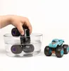A child's hand is shown dipping a black monster truck toy into a clear bowl of water, while a blue monster truck toy sits to the right on a white background. Voir les images du produit