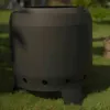A black, cylindrical fire pit with three legs sits on a grassy lawn. Anteprima dell’immagine prodotto
