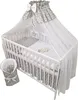 A white wooden crib with grey and white star-patterned bedding and a canopy. Produktbild-Vorschau