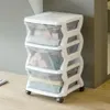 A white and transparent plastic drawer unit with three drawers, shown on a wooden floor next to a gray wall. Anteprima dell’immagine prodotto
