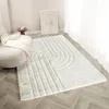 A cream-colored rug with a raised geometric pattern is laid out on a wooden floor in a room with a chair and a framed picture. Produktbild-Vorschau
