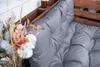 A close-up view of a grey cushion on a wooden pallet bench, with dried flowers in the foreground. Produktbild-Vorschau