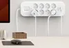 A white power strip with multiple outlets and USB ports is mounted on a wall above a desk. Cables are plugged into the outlets, and a mouse and headphones are on the desk. Náhled obrázku produktu