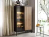 A modern display cabinet with glass doors and a slatted wood panel, showcasing illuminated interior shelves, stands next to sheer curtains and a window. Náhled obrázku produktu