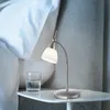 A bedside table with a glass of water and a silver LED table lamp with a white glass shade. Produktbild-Vorschau