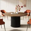 A round dining table with a wooden top and a fluted black base, surrounded by four orange chairs in a well-lit room. Produktbild-Vorschau