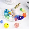 A collection of colorful glass marbles arranged on a white plate with a decorative bunny figurine. Náhľad obrázku produktu