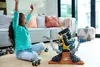 A young girl is playing with a Hot Wheels Monster Trucks Arena World Championship playset on the floor in a living room. Produktbild-Vorschau