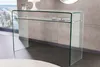 A modern glass console table with a shelf, placed in a room with a large window and a textured wall. Produktbild-Vorschau
