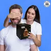A woman surprises a man with a gift box, covering his eyes. Produktbild-Vorschau