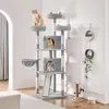 A multi-level cat tree with several platforms, cubbies, and a hanging basket, occupied by two cats. The cat tree is placed in a room with a white wall and a light-colored floor. Decorative wall hangings and a small cat toy are visible on the right side of  Podgląd zdjęcia produktu