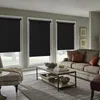 A living room scene with three black roller blinds covering windows, a sofa, coffee table, and armchair. Produktbild-Vorschau