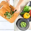 A person is chopping cucumbers on a wooden cutting board, with a digital kitchen scale and other vegetables in the background. Produktbild-Vorschau