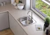 A kitchen sink with a faucet on a countertop next to a window with greenery outside. Produktbild-Vorschau