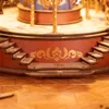 A close-up view of a wooden carousel model, focusing on the decorative base and stairs. Produktbild-Vorschau