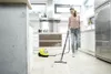 A woman is cleaning a kitchen floor with a steam cleaner. Produktbild-Vorschau