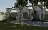 A backyard scene with a wooden pergola covered in white drapes, furnished with a table and chairs, set against a backdrop of greenery and a stone wall. Produktbild-Vorschau