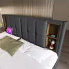 A bed with a headboard featuring built-in shelves, a tablet, and decorative items. Náhled obrázku produktu