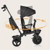 A black Lionelo Kori tricycle is shown against a light beige background, with orange arrows indicating rotation and movement. Produktbild-Vorschau