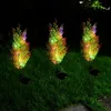 Three solar-powered cypress tree lights are illuminated with colorful LEDs in a grassy yard at night. Anteprima dell’immagine prodotto