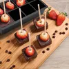Chocolate-covered strawberries and chocolate chips arranged on a wooden board, with a silicone ice cube mold in the background. Náhled obrázku produktu