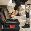 A person is using an angle grinder on a concrete staircase, with a tool case open in the foreground. Náhled obrázku produktu