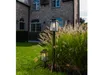 Two outdoor lanterns are placed in a garden next to a brick building. Produktbild-Vorschau
