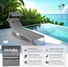 A grey sun lounger is placed on a patio next to a swimming pool with a tropical background. Náhled obrázku produktu