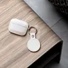 A white AirTag holder and a clear case for wireless earbuds are placed on a wooden surface. Voir les images du produit