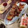 A platter of grilled meat skewers with red peppers and a jar of mustard, served with two small bowls of dipping sauces on a wooden board. Produktbild-Vorschau