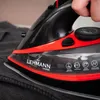Close-up of a person's hand using a black and red steam iron on dark fabric. Voir les images du produit