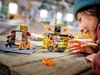 A young girl is playing with a LEGO stunt park set on a wooden table. Podgląd zdjęcia produktu