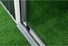 A close-up view of the bottom edge of a metal shed, showing the track and the green artificial grass surrounding it. Produktbild-Vorschau