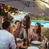 People enjoying a meal outdoors under a large umbrella with string lights. Náhled obrázku produktu