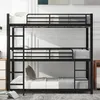 A triple bunk bed with black metal frame and white bedding is shown in a room with white walls and a patterned rug. Produktbild-Vorschau
