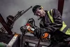 A construction worker is using an angle grinder on a construction site with a crane in the background. Voir les images du produit