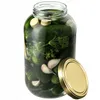 A glass jar filled with pickles, dill, and garlic, with its gold lid placed next to it. Podgląd zdjęcia produktu