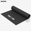 A black yoga mat is partially unrolled on a white background, with the brand logo visible. Produktbild-Vorschau