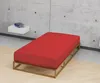 A red mattress on a wooden bed frame against a concrete wall. Produktbild-Vorschau